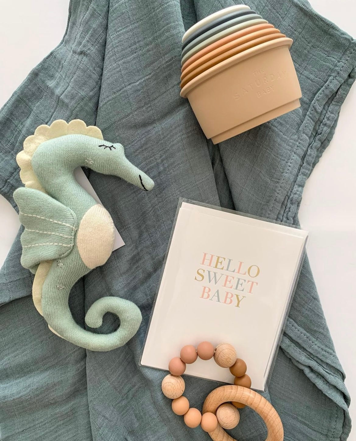 baby gift made up of blue steel muslin swaddle, seahorse soft toy, silicone baby teether, silicone stacking cups and greeting card