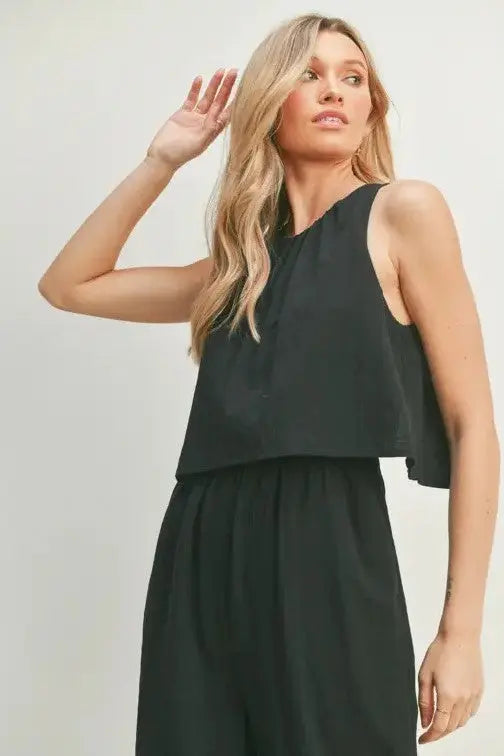 A female model showcasing a black wide-leg sleeveless jumpsuit