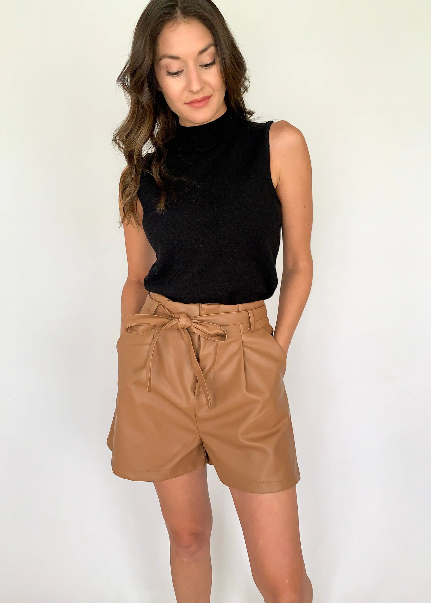 A female model dressed in a black top and large size camel leather shorts with a belt