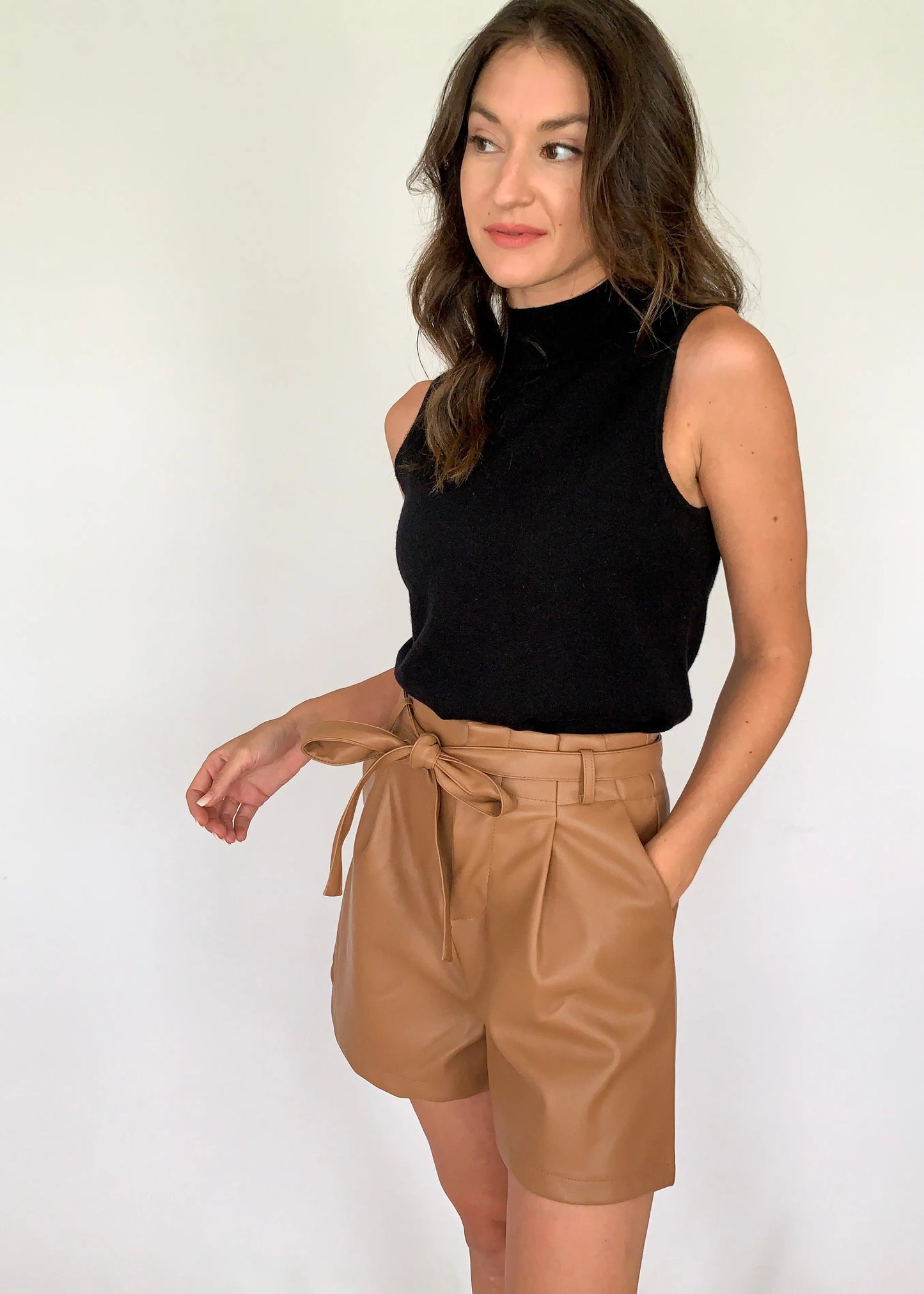 A female model dressed in a black top and large size camel leather shorts with a belt