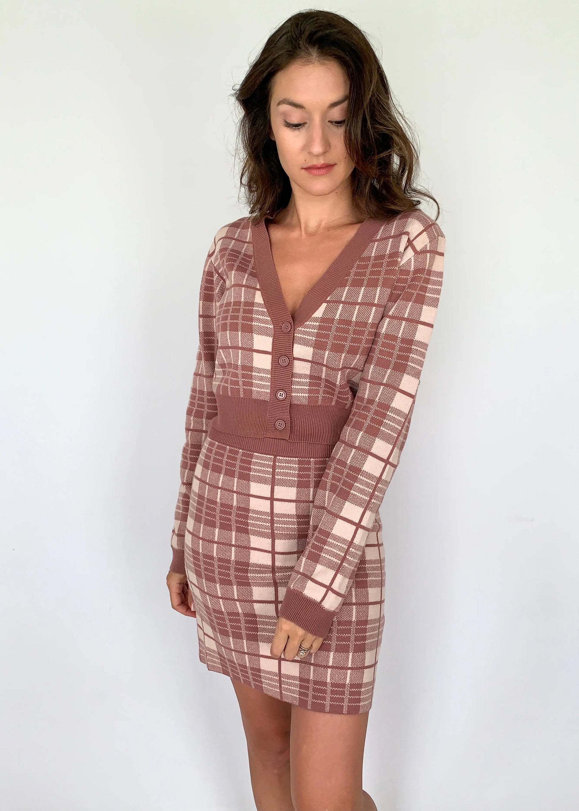 A model wearing a mauve plaid v-neck cropped cardigan with matching skirt